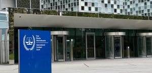 The exterior of a glass building with a blue sign that says 'International Criminal Court' outside.