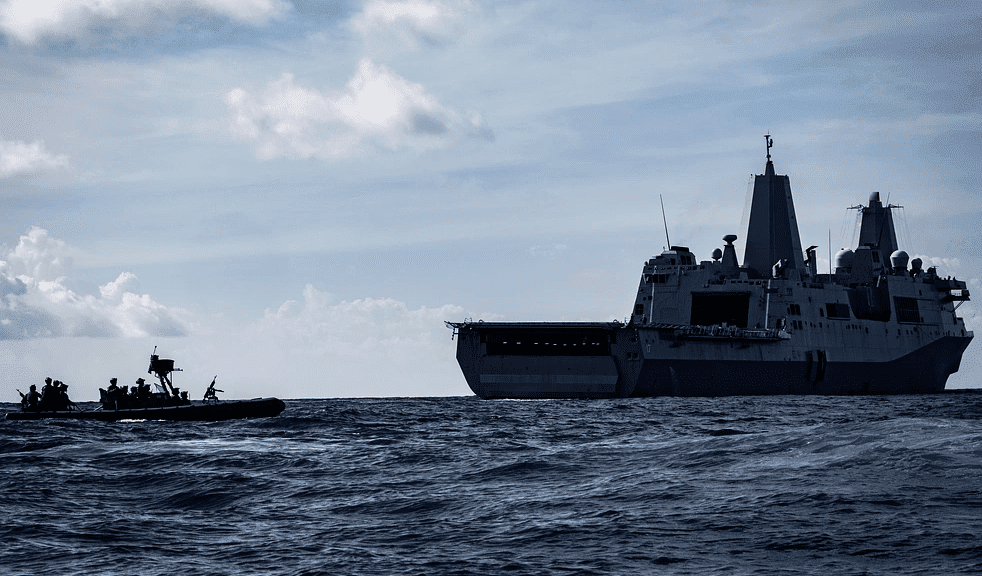 Large gray warships at sea under a blue sky streaked with white clouds.