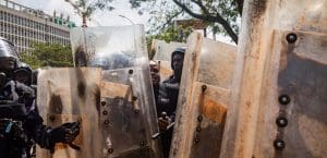 A row of riot police shields with uniformed cops behind them in heavy protective gear.