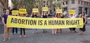 A group of protesters holding a large, yellow horizontal banner that says 
