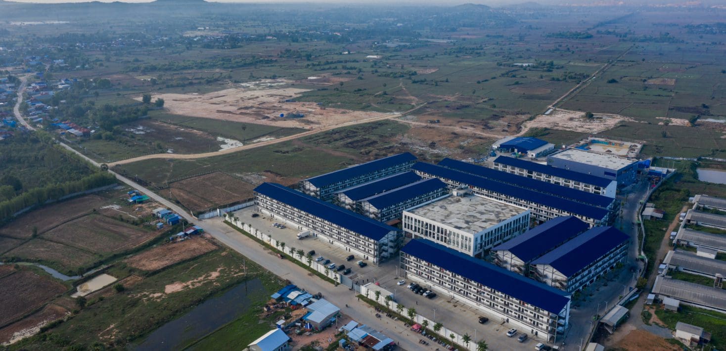 An overhead view of a large compound surrounded by walls and fields, connected by a single road to a nearby town.