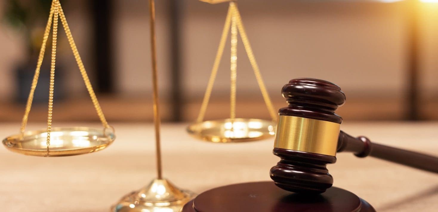 A dark brown gavel lies next to a brass Lady Justice balance scale.