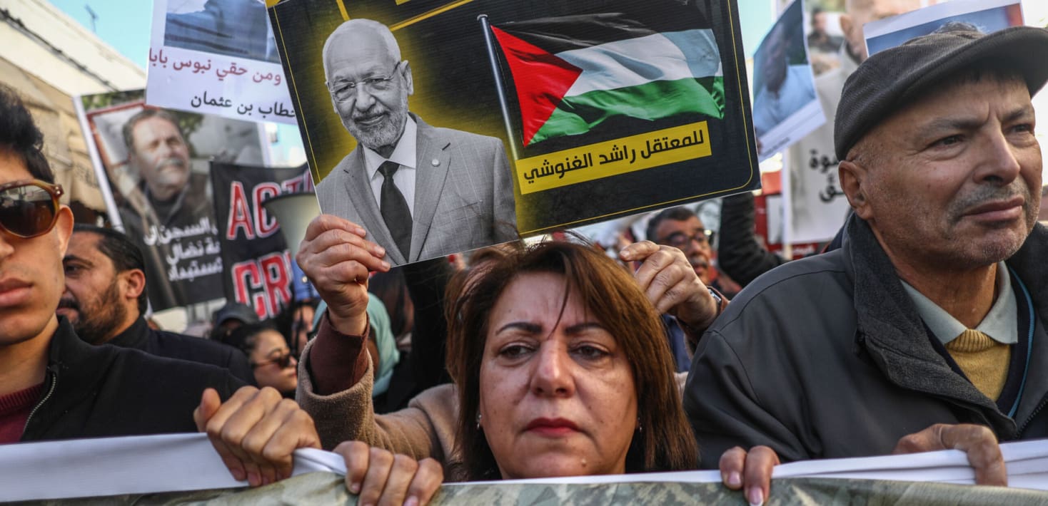 A crowd of people with solemn faces march with signs and banners.