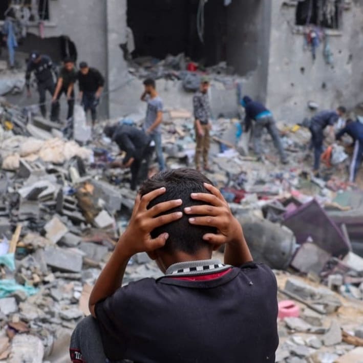 young boy in front of destroyed building in Gaza