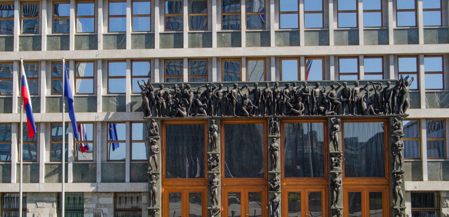 An exterior of the Slovenian national assembly building. A glass building with a large brown frieze.