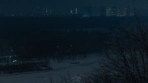 Photograph of an electricity blackout in Ukraine. All dark/black with a slight silhouette of a city landscape in the background.