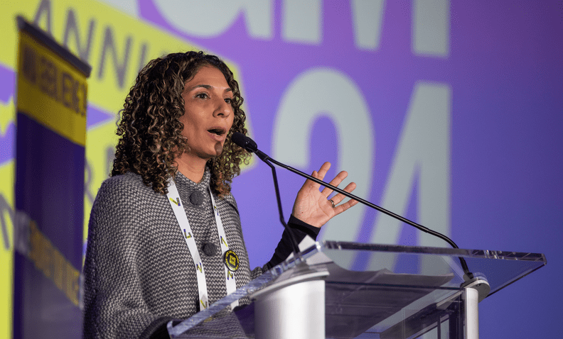 Nadia Daar speaking in front of amnesty international sign purple and yellow