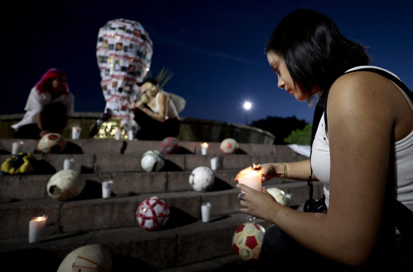 A student from the Jesuit University of Guadalajara (ITESO) places a candle near a replica of the FIFA World Cup trophy decorated with pictures of missing persons, during an art intervention with the 