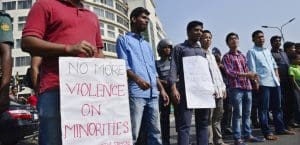 A handful of men protesting in Bangladesh. One is holding a sign that reads 'No More Violence on Minorities'