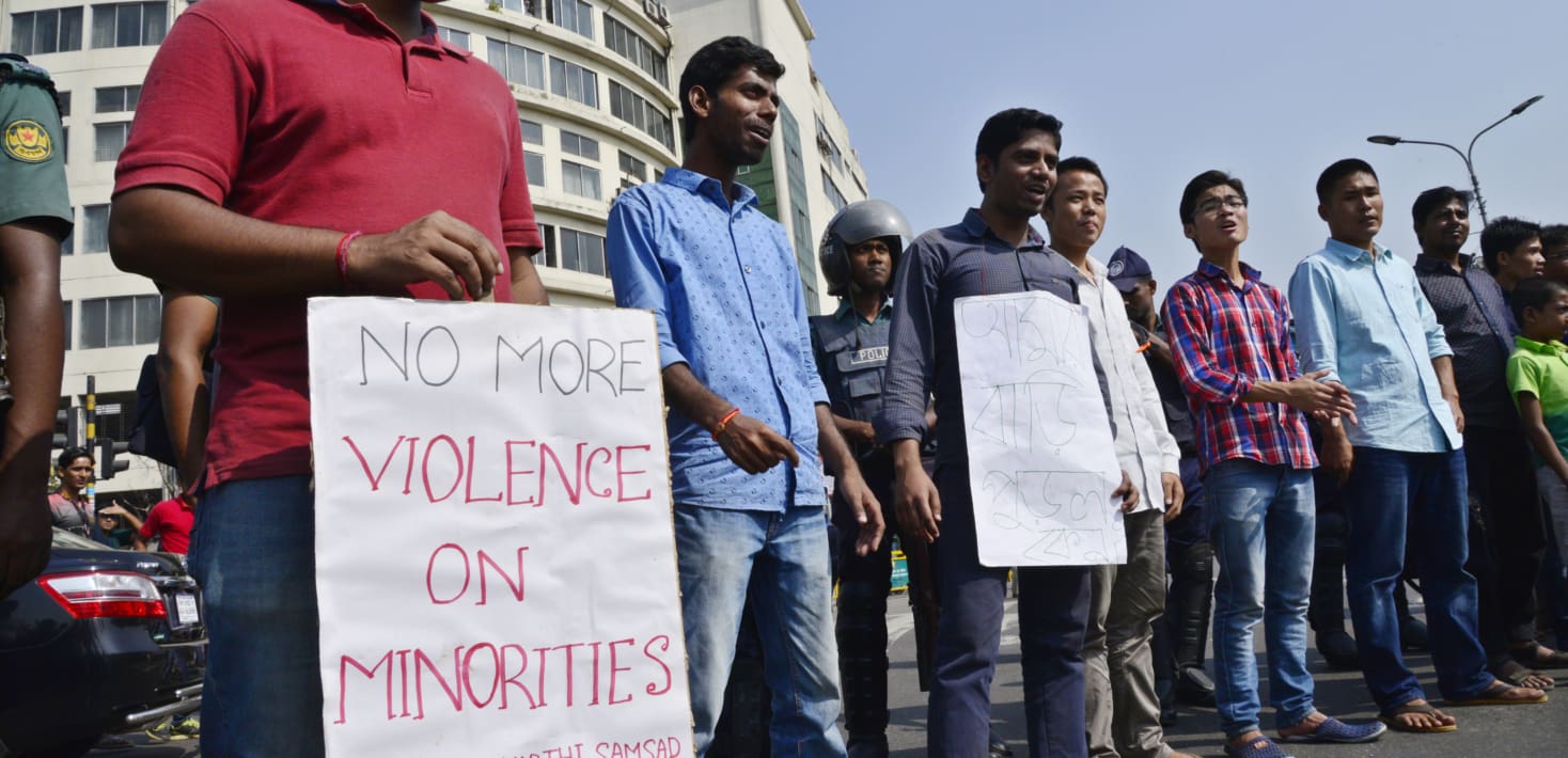 A handful of men protesting in Bangladesh. One is holding a sign that reads 'No More Violence on Minorities'