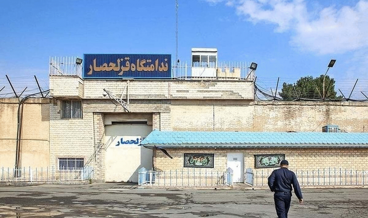 A white brick building with barbed wire and a sign written in Farsi.
