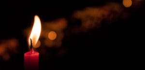 A photograph of a lit red candle, with a black backdrop.