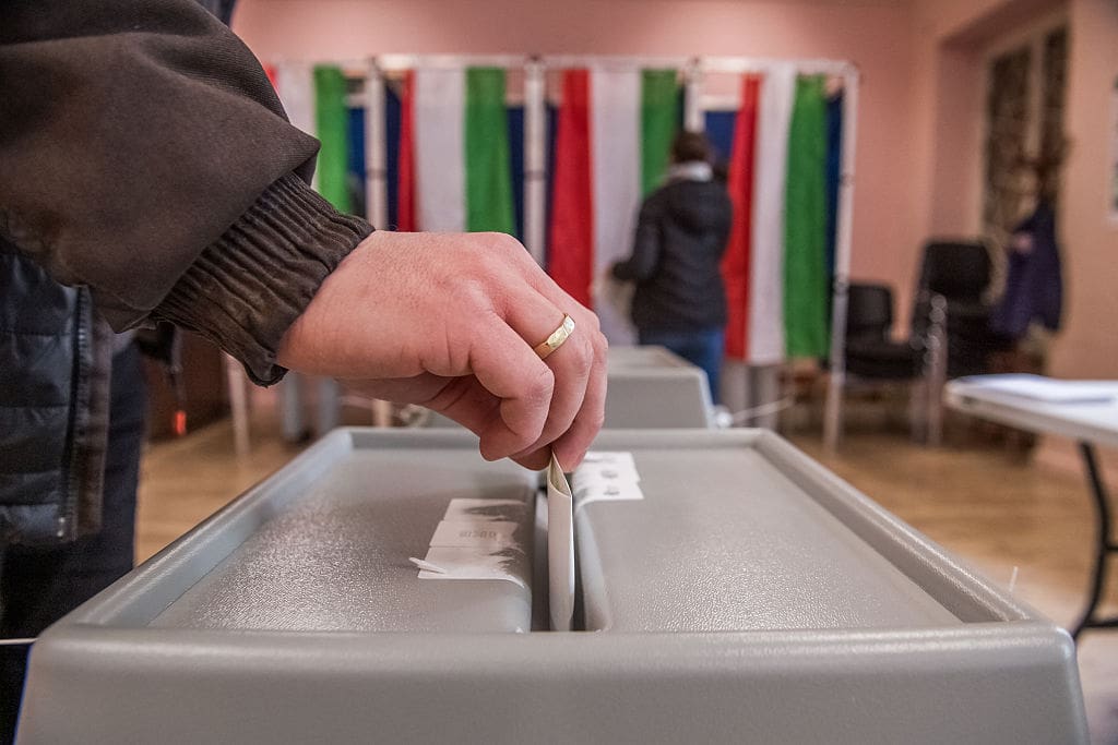A close-up photograph of a hand putting a ballot in a ballot box.