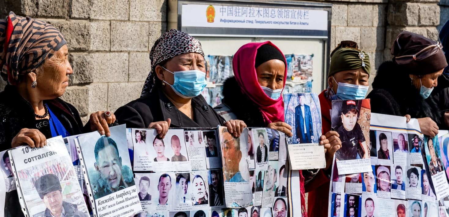 Five women in hijab holding photographs of young men.