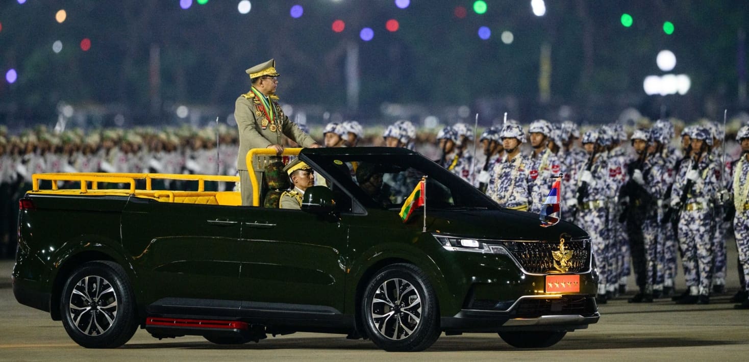 A military parade with a general standing at front, in a black car.