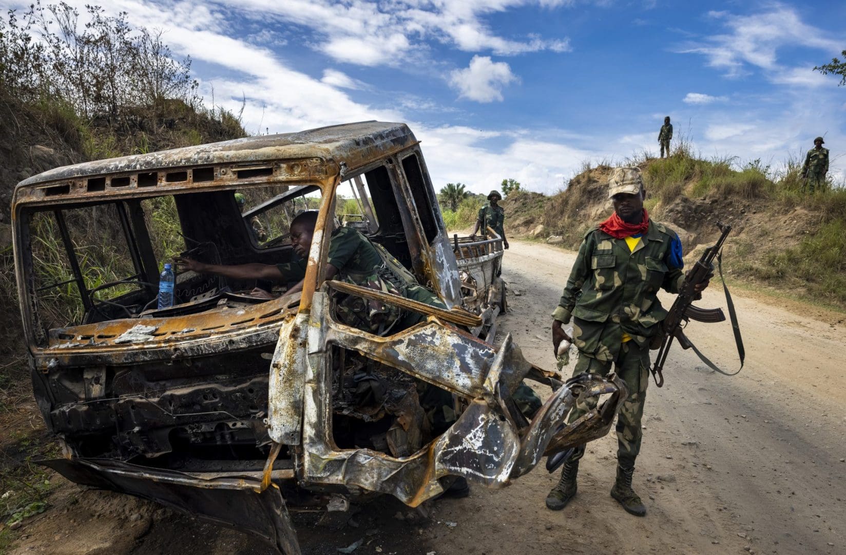 Armed Congolese soldiers inspect the charred shell of a minibus.