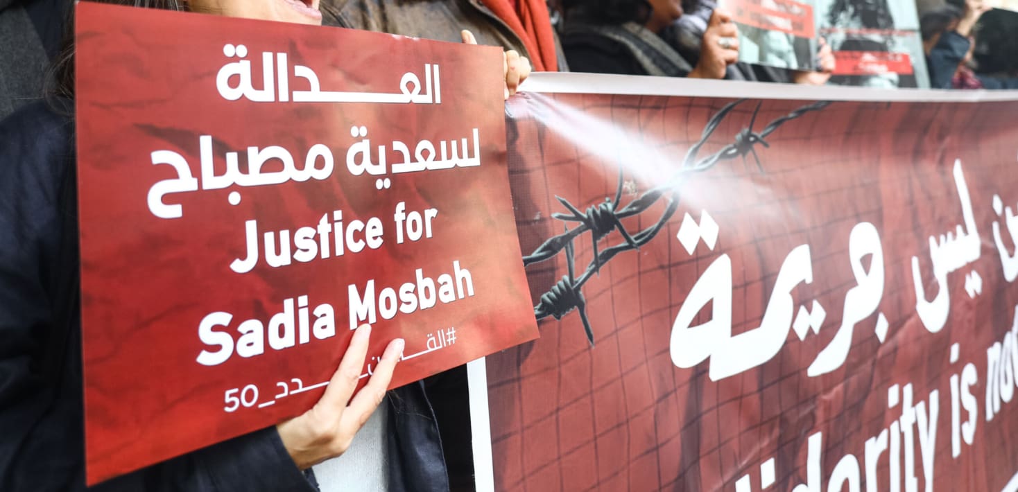 Activists hold a red and black banner depicting barbed wire and words reading 