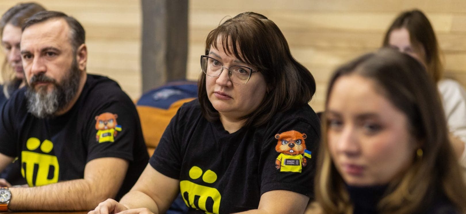 three people sit at a table wearing black tshirts wth Amnesty International logos