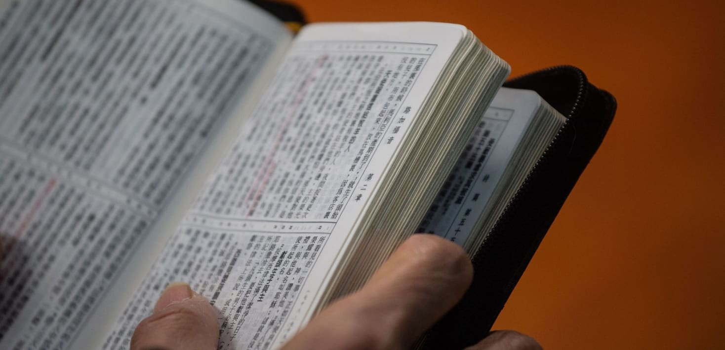 A close up view of a Bible in Chinese language, held open by two hands.