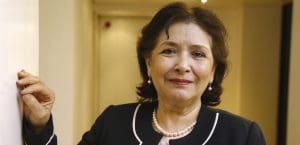 Sihem Bensedrine poses for a portrait in a hallway, wearing a slight smile and a black suit and earrings.