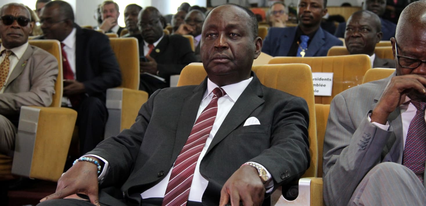 Francois Bozize with a bored look on his face sits in the front row of a conference hall full of people seated behind him wearing a suit and tie.