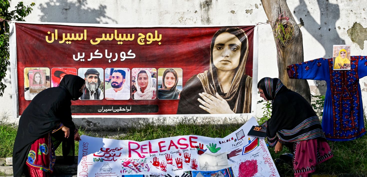 A red banner hung between two trees. The banner features several photographs of people.