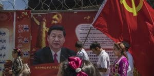 People walk past a red banner with a picture of Ji Xinping on a busy street.