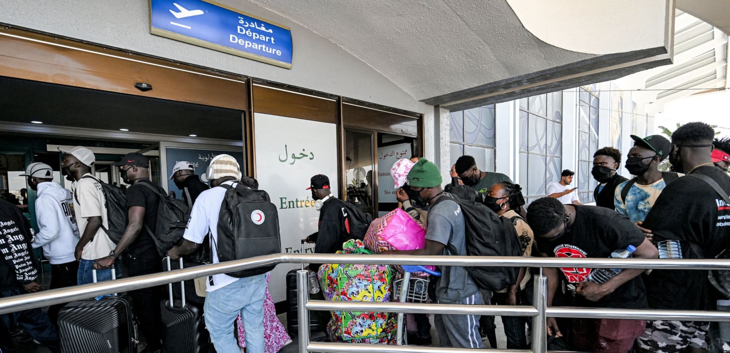 People line up with belongings at an airport terminal.