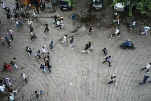 Seen from above, people run across open pavement, scattering in different directions.