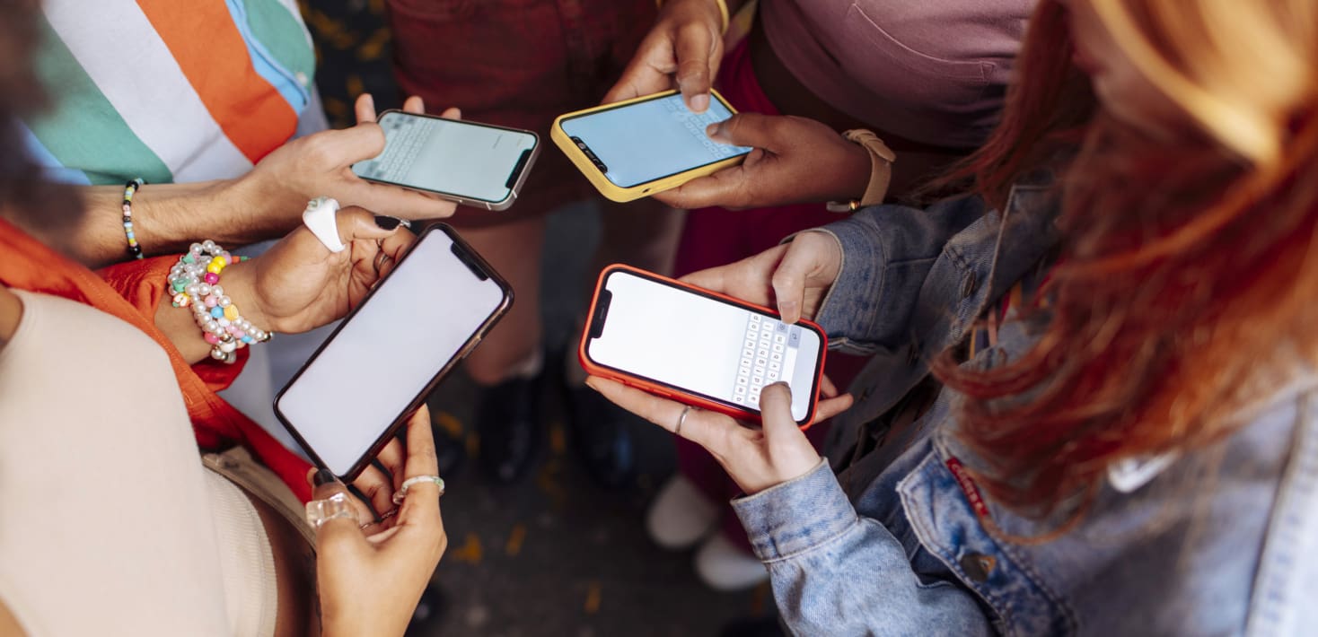 Four people wearing bright colored clothing and bracelets hold cell phones.