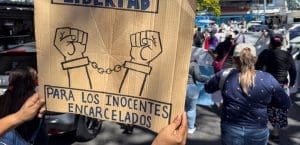 A woman displays a banner during a march to the Supreme Court of Justice to demand that the state of exception imposed by President Nayib Bukele in his 'war' against gangs —which allows arrests without warrants— be declared unconstitutional, in San Salvador on November 11, 2025. Since March 2022, Bukele has used a state of emergency to jail gang members and collaborators. More than 89,000 people have been detained and about 8,000 released after being found innocent, according to official sources. (Photo by Rudy QUIROZ / AFP)