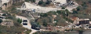 Green military trucks drive through a landscape of rubble.