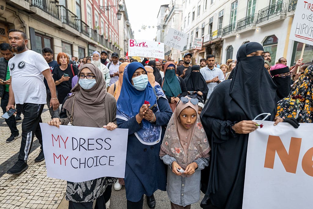 Female protesters wearing burkas march with placards.