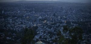 A darkened city after dusk, with only a few lights on buildings. In the distant blue haze, a rough horizon. Quiet.