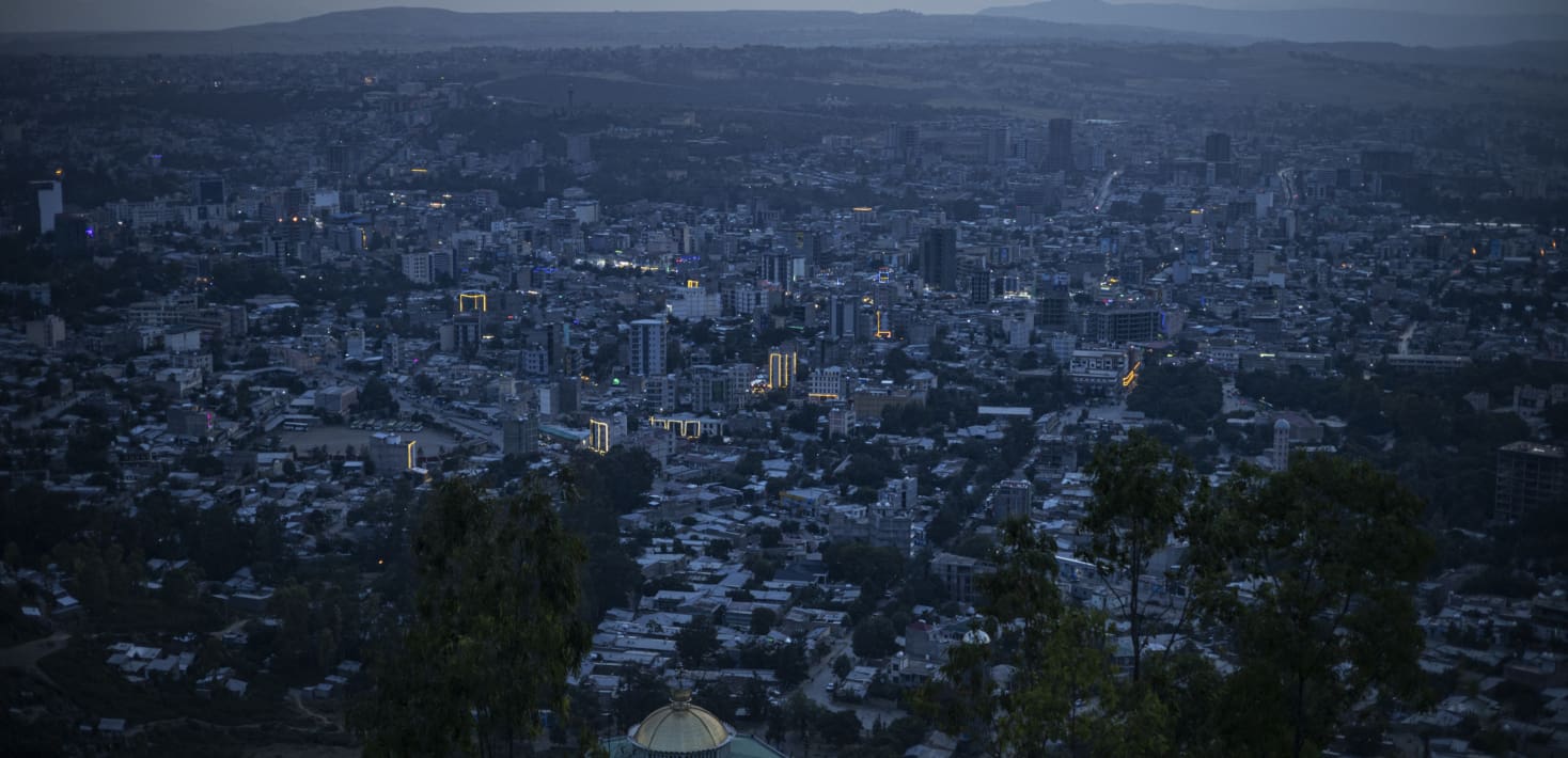 A darkened city after dusk, with only a few lights on buildings. In the distant blue haze, a rough horizon. Quiet.