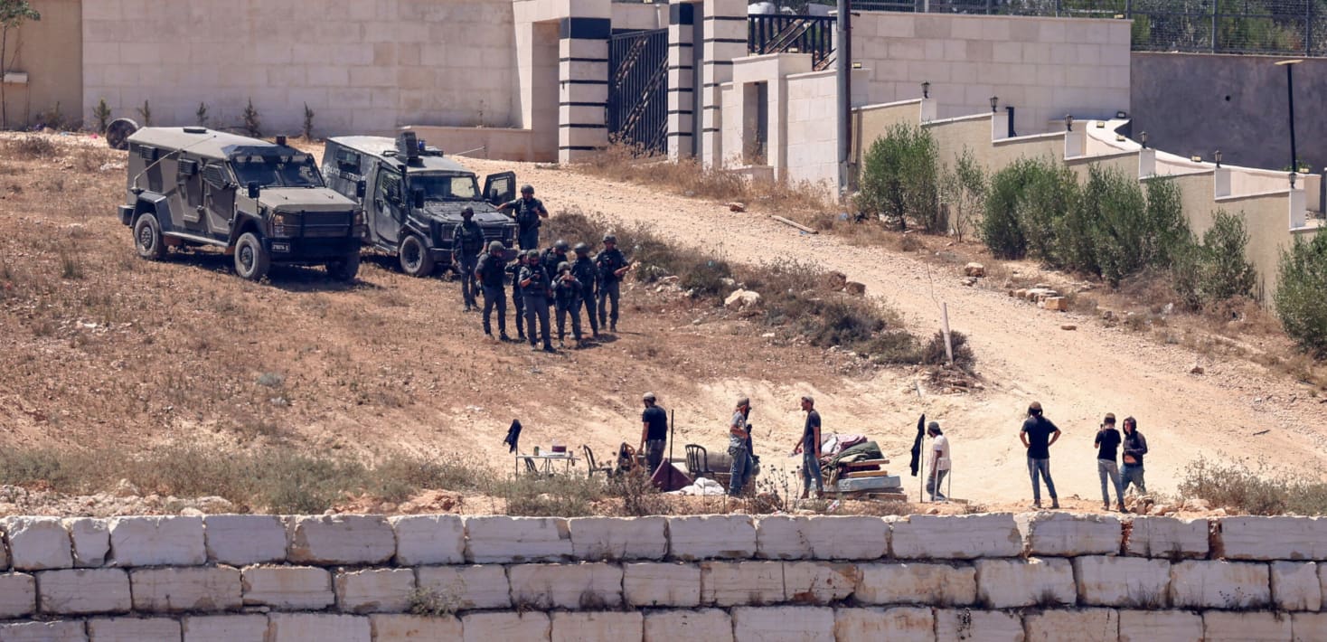 Israeli troops and settlers standing outside a home.