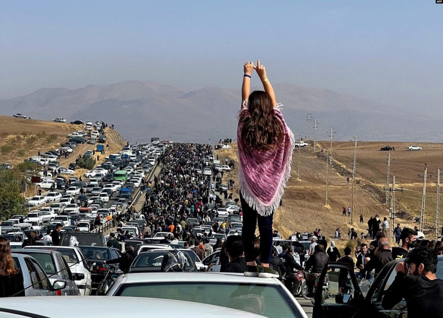This October 26 2022, dated image posted on Twitter shows an unveiled woman standing on top of a vehicle as thousands make their way toward Aichi cemetery in Saqez, Mahsa Amini's hometown in the western Iranian province of Kurdistan, to mark 40 days since her death.
