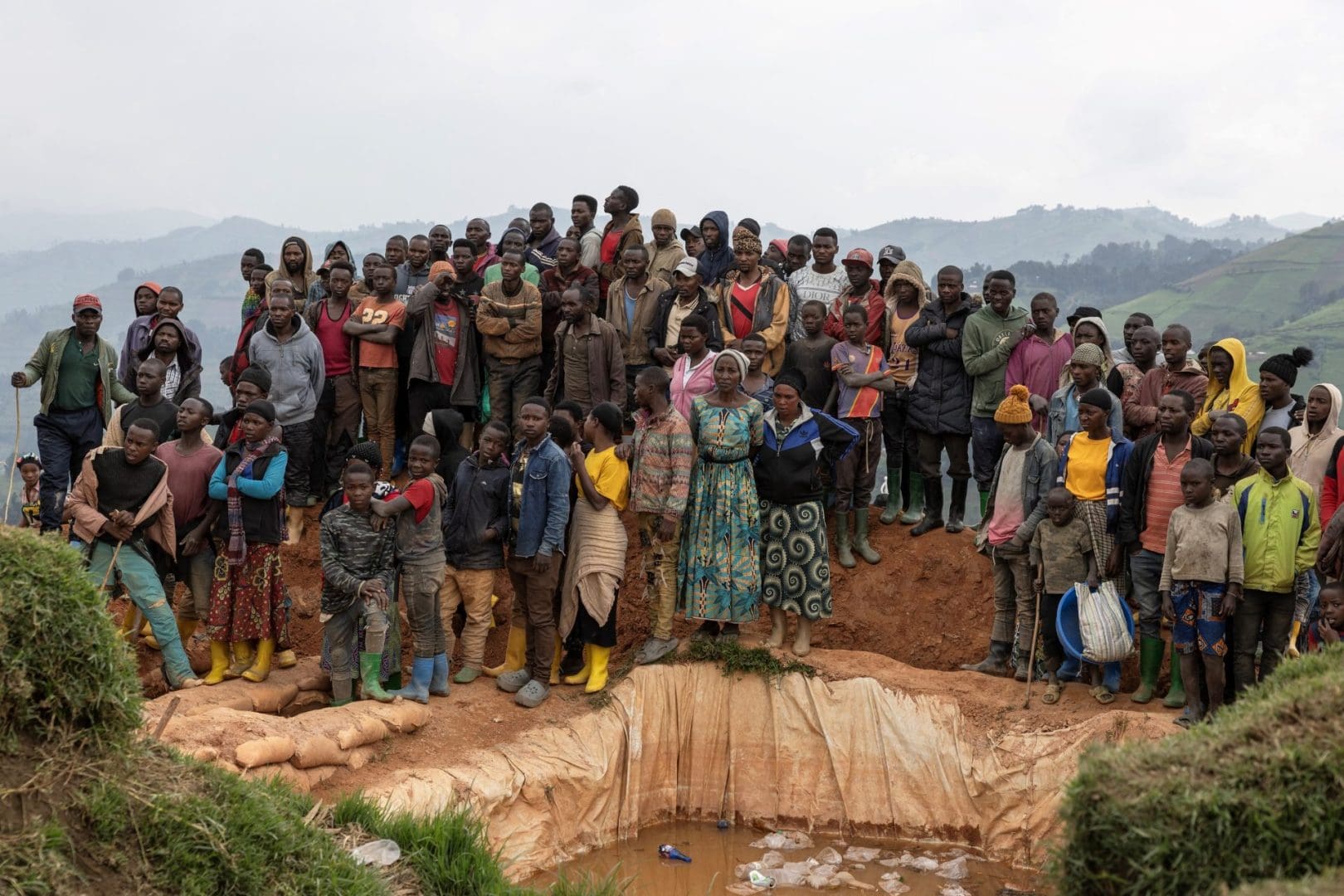 Civilians stand crowded on a small hilltop above a mine shaft.