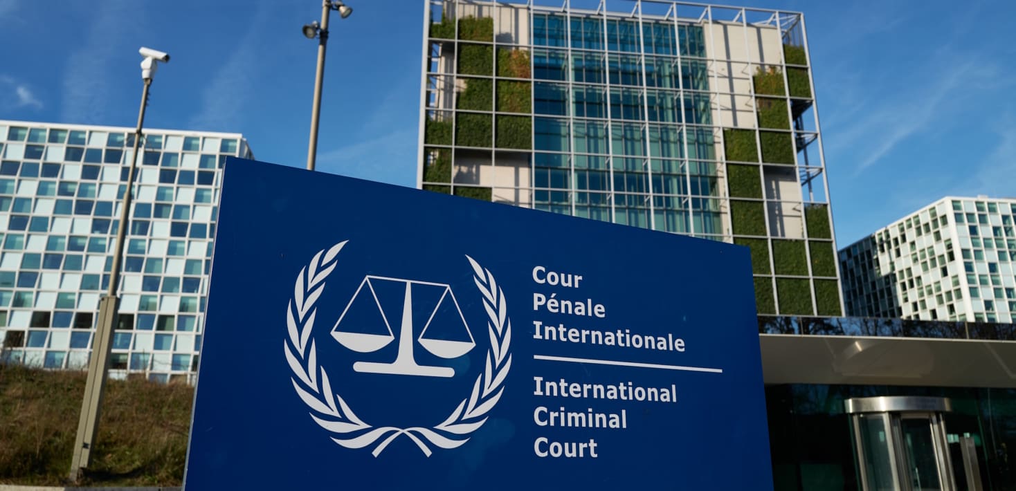 A blue International Criminal Court sign with the ICC logo in front of a complex of buildings with lots of windows. It is in the Hague. It is the ICC.