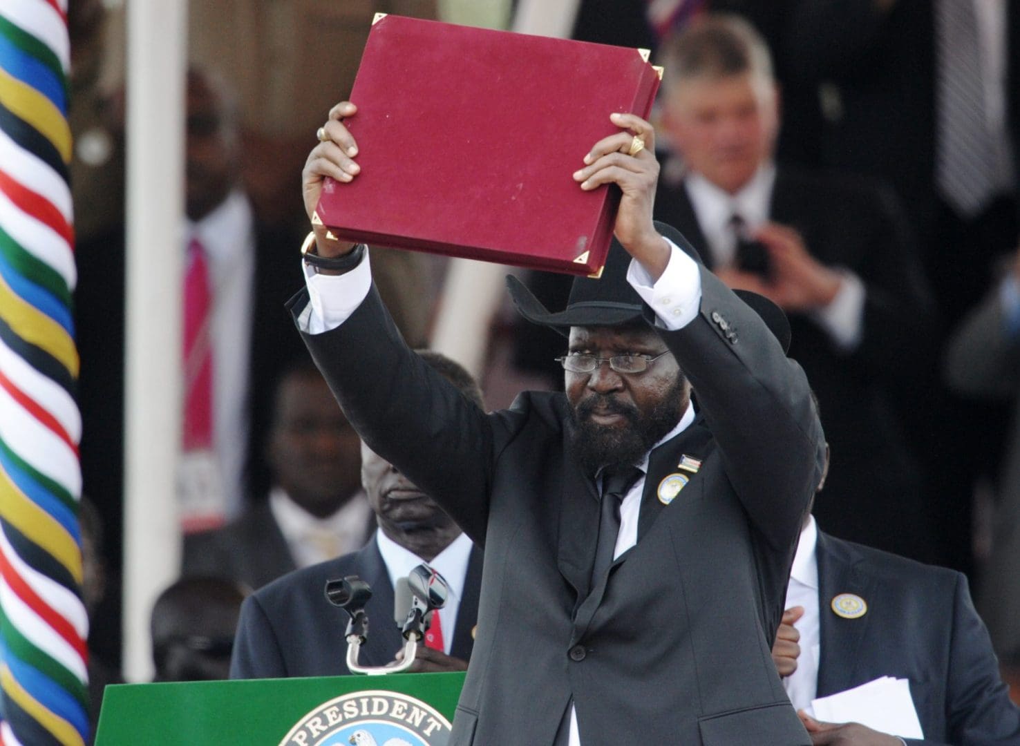 A man in a black suit and a black cowboy hat holds a book over his head.