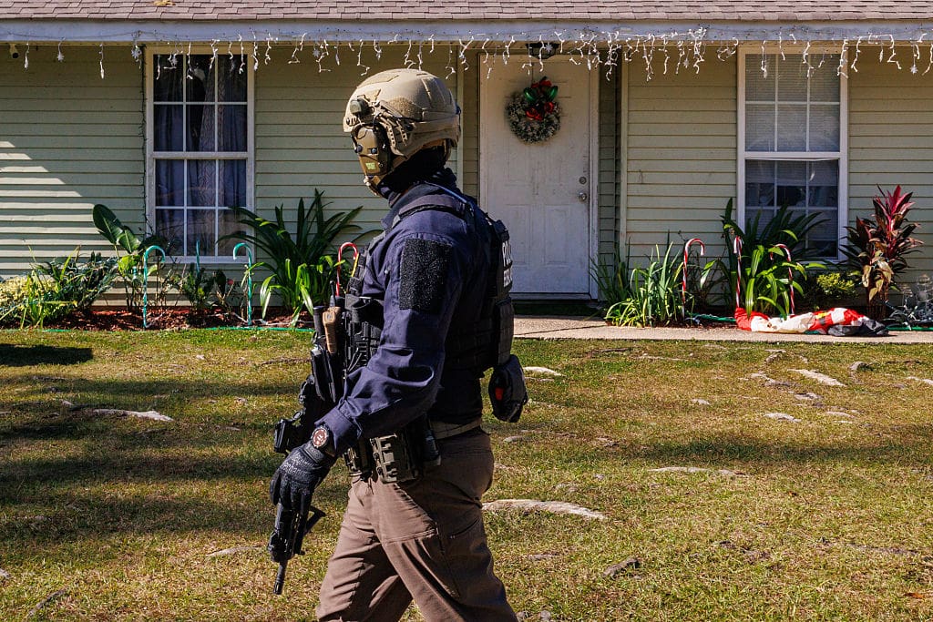 An armed federal agent walks past a home adorned with holiday decorations while enforcing federal immigration operations in Covingston, Louisiana, United States, on December 11, 2025.