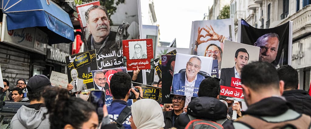 People protest down a narrow street holding up signs of the convicted people.