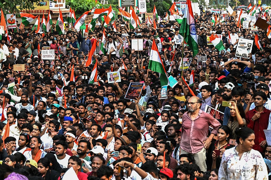 A large crowd of people, mostly men, tightly packed holding Indian flags and signs.